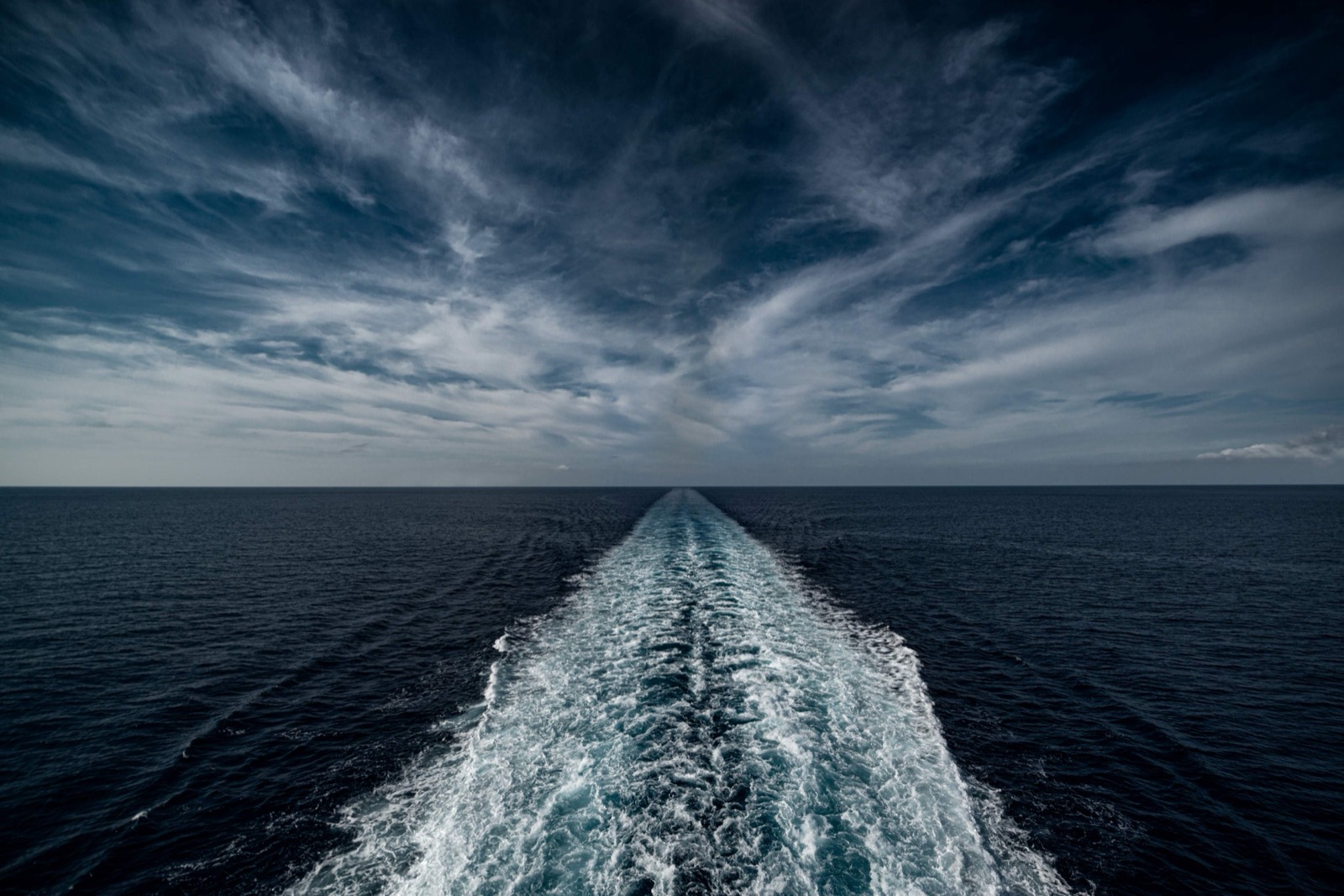 A vessel's wake stretching to the horizon under a dramatic sky