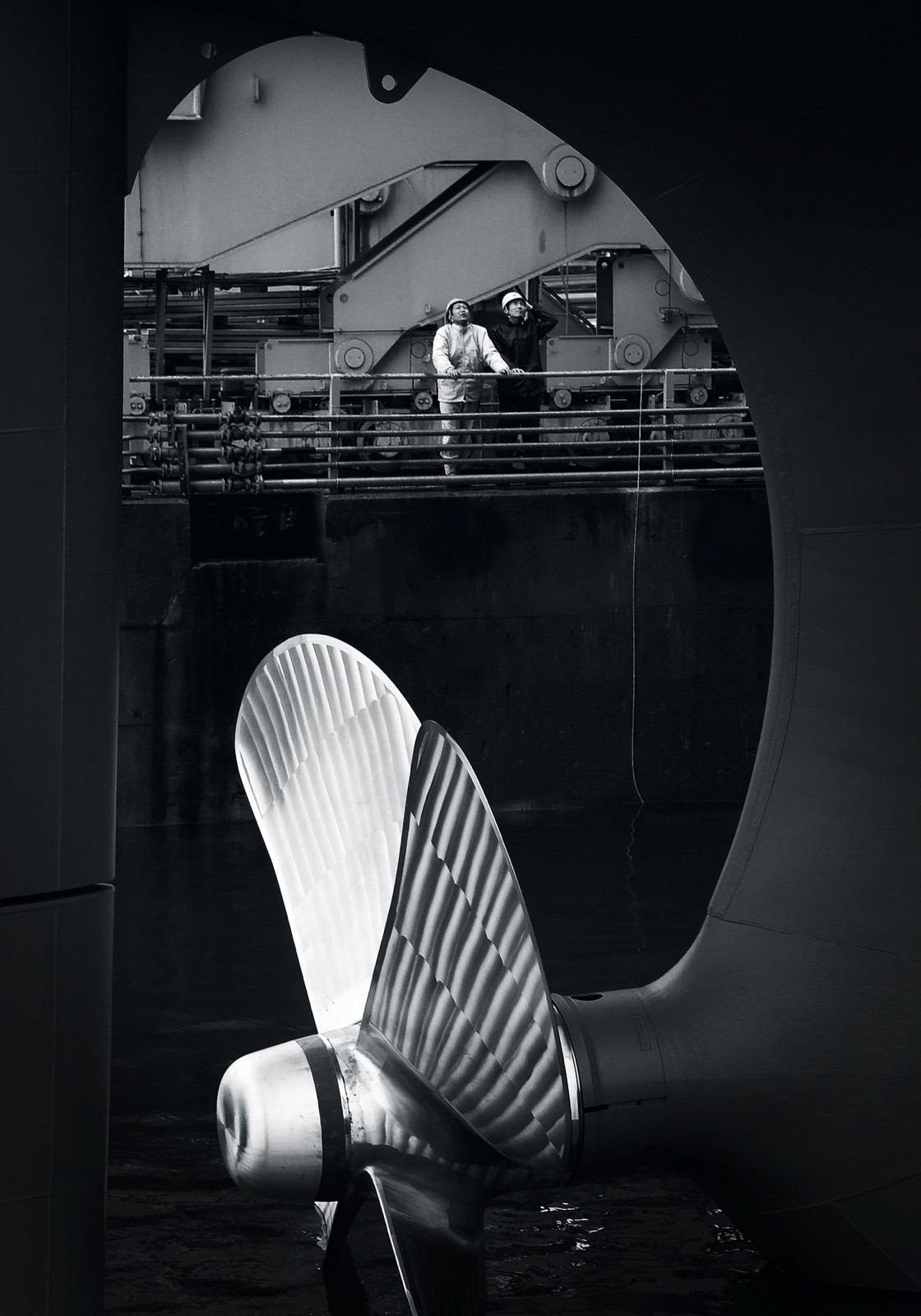 Two crew in hi-vis beside a ship's propeller in dry dock