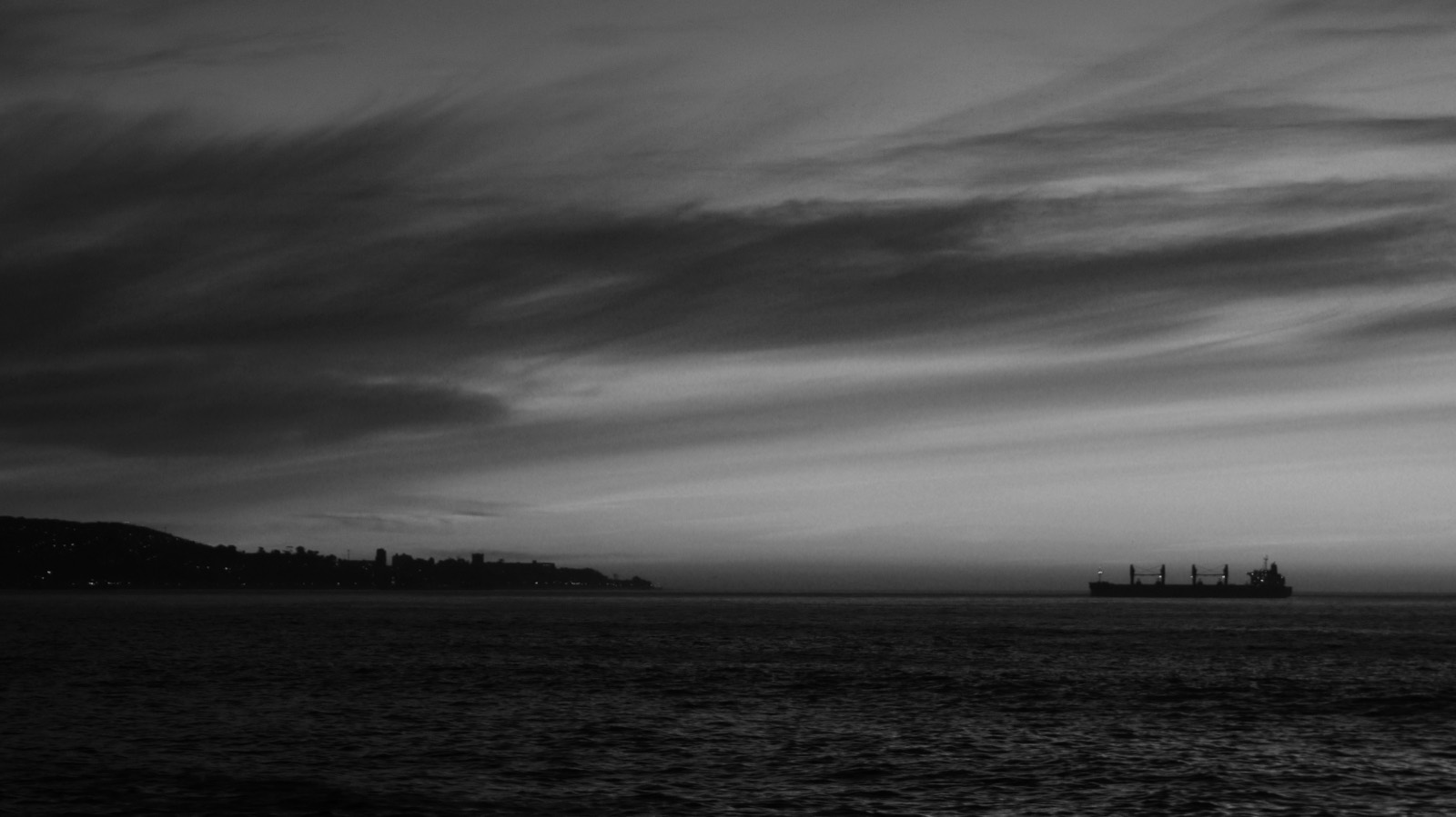 A cargo vessel on the horizon at dusk off a coastline