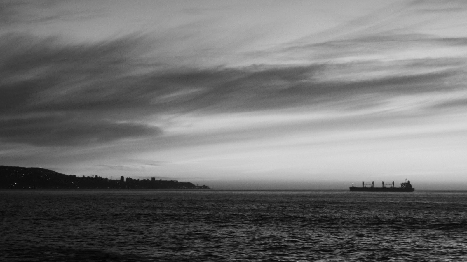 A cargo vessel at anchor on the horizon at dusk