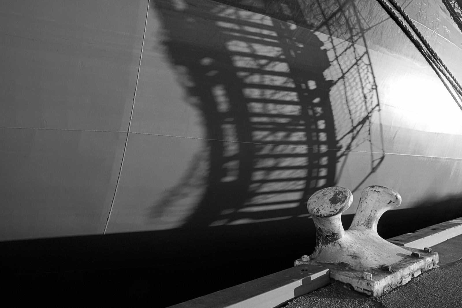 A ship's hull alongside a quay with a mooring bollard in the foreground